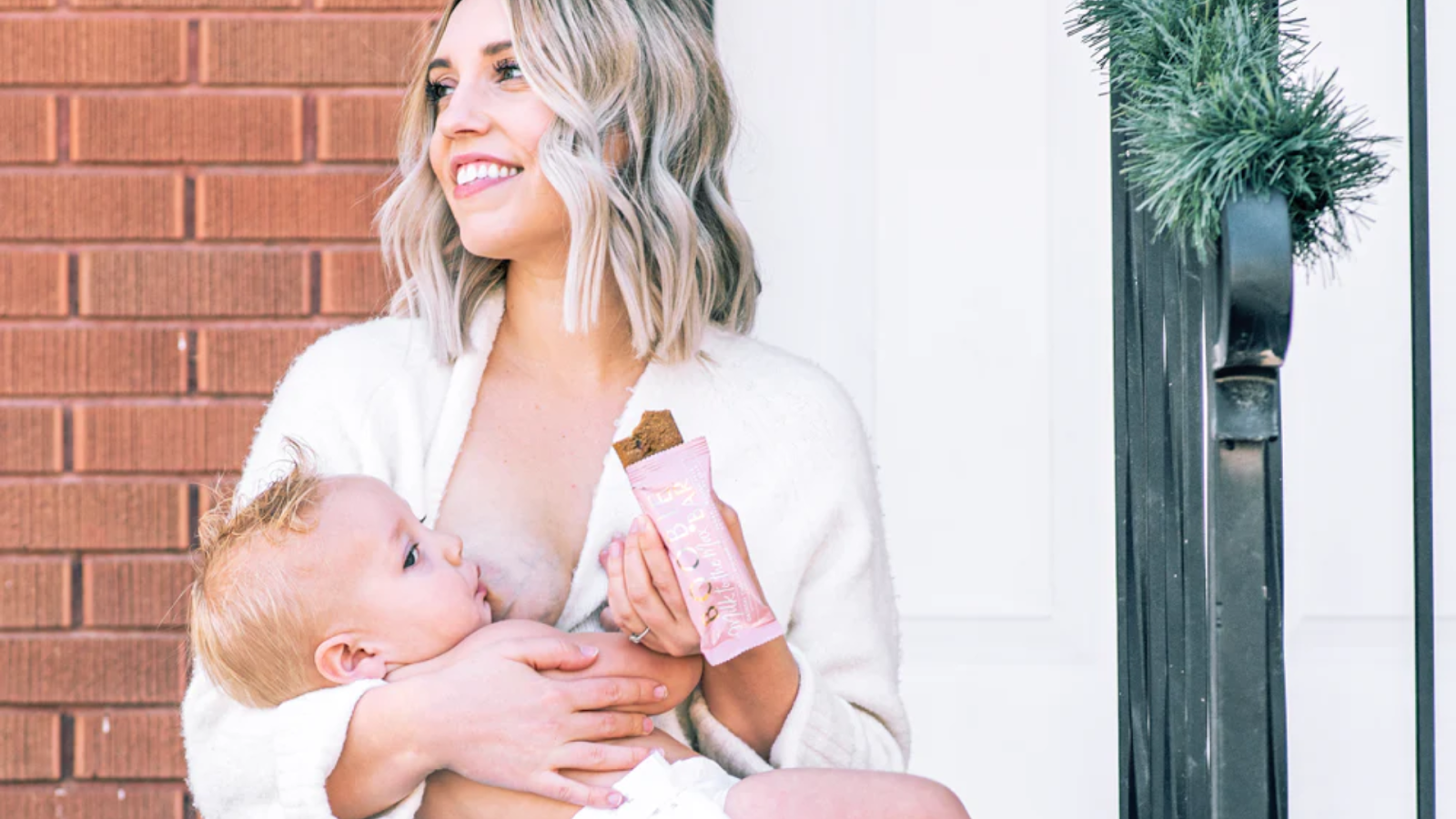 Breastfeeding mom using a BOOBIE lactation bar to stay nourished during a nursing session.
