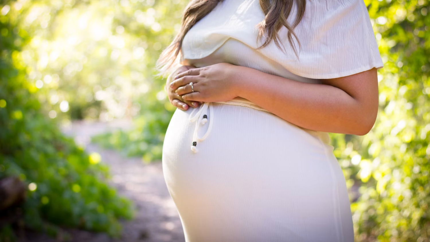 Close-up of a pregnant belly in a sunlit outdoor setting.