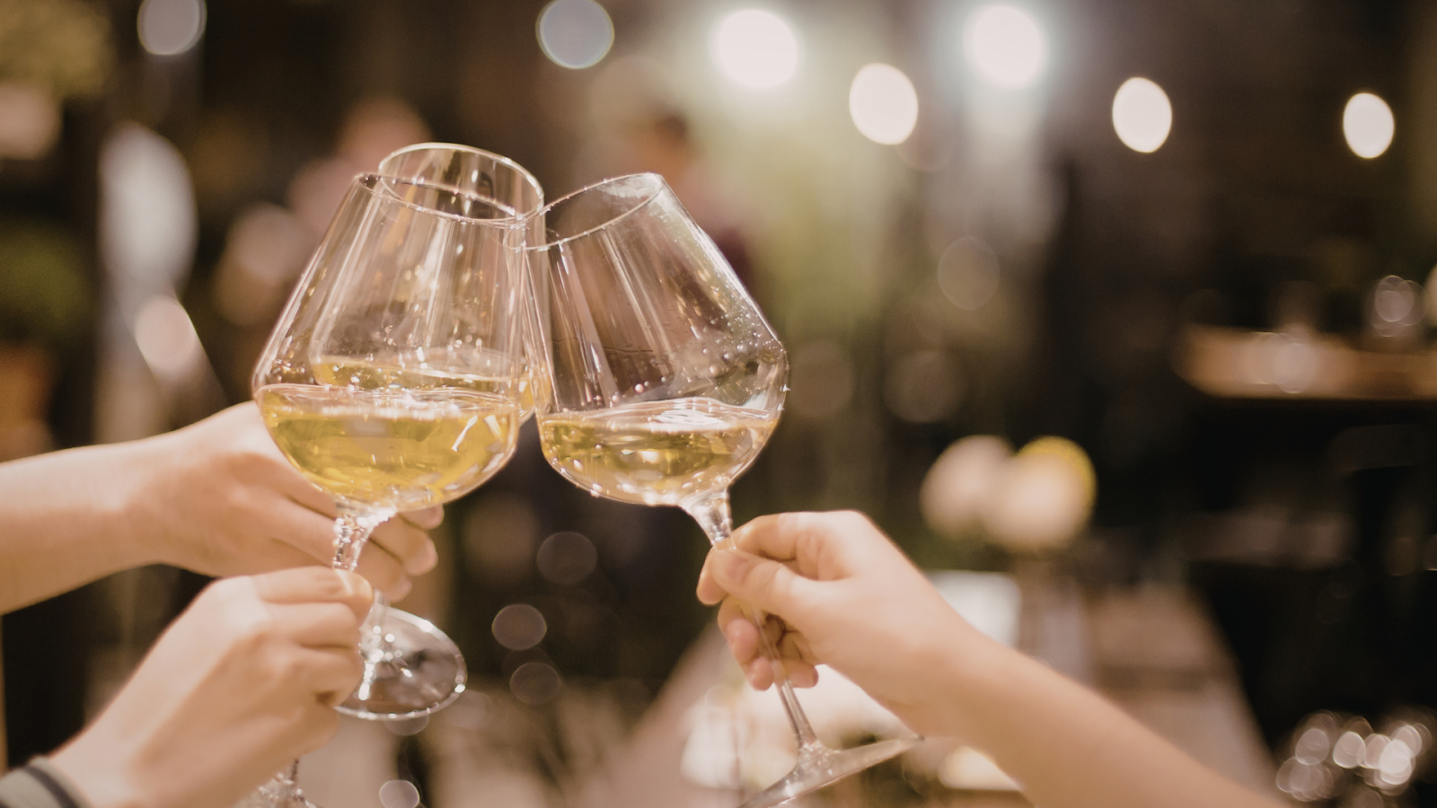 Hands clinking glasses of white wine during a dinner toast.