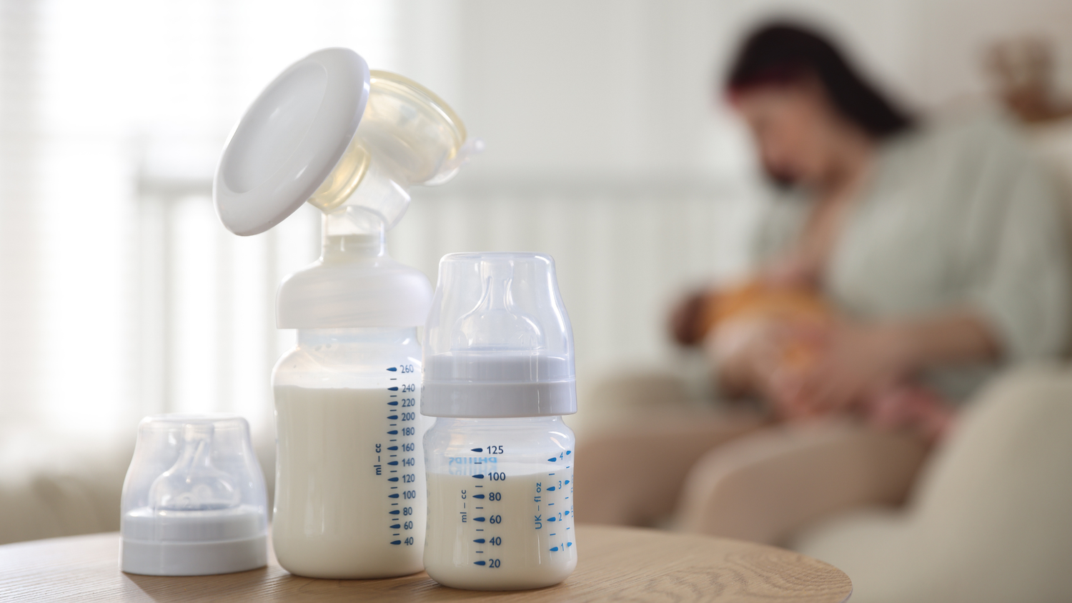 Manual breast pump and milk bottles with nursing mother behind