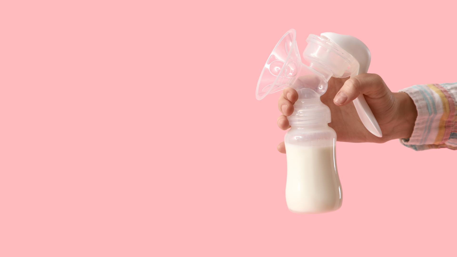 Manual breast pump filled with stored breastmilk on pink background