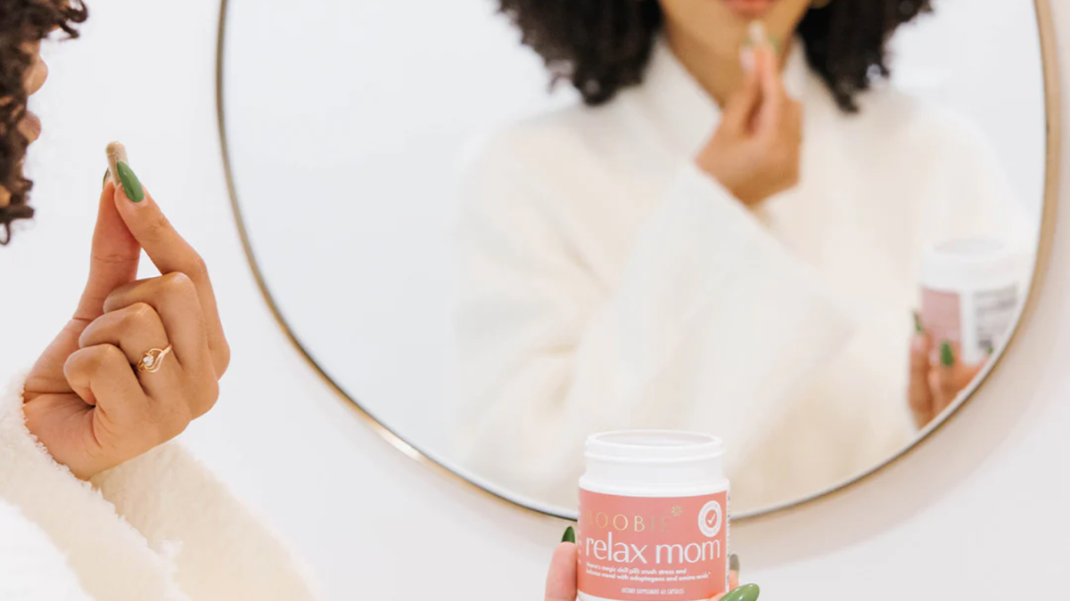 Mom holding a Boobie Relax Mom supplement in front of a mirror