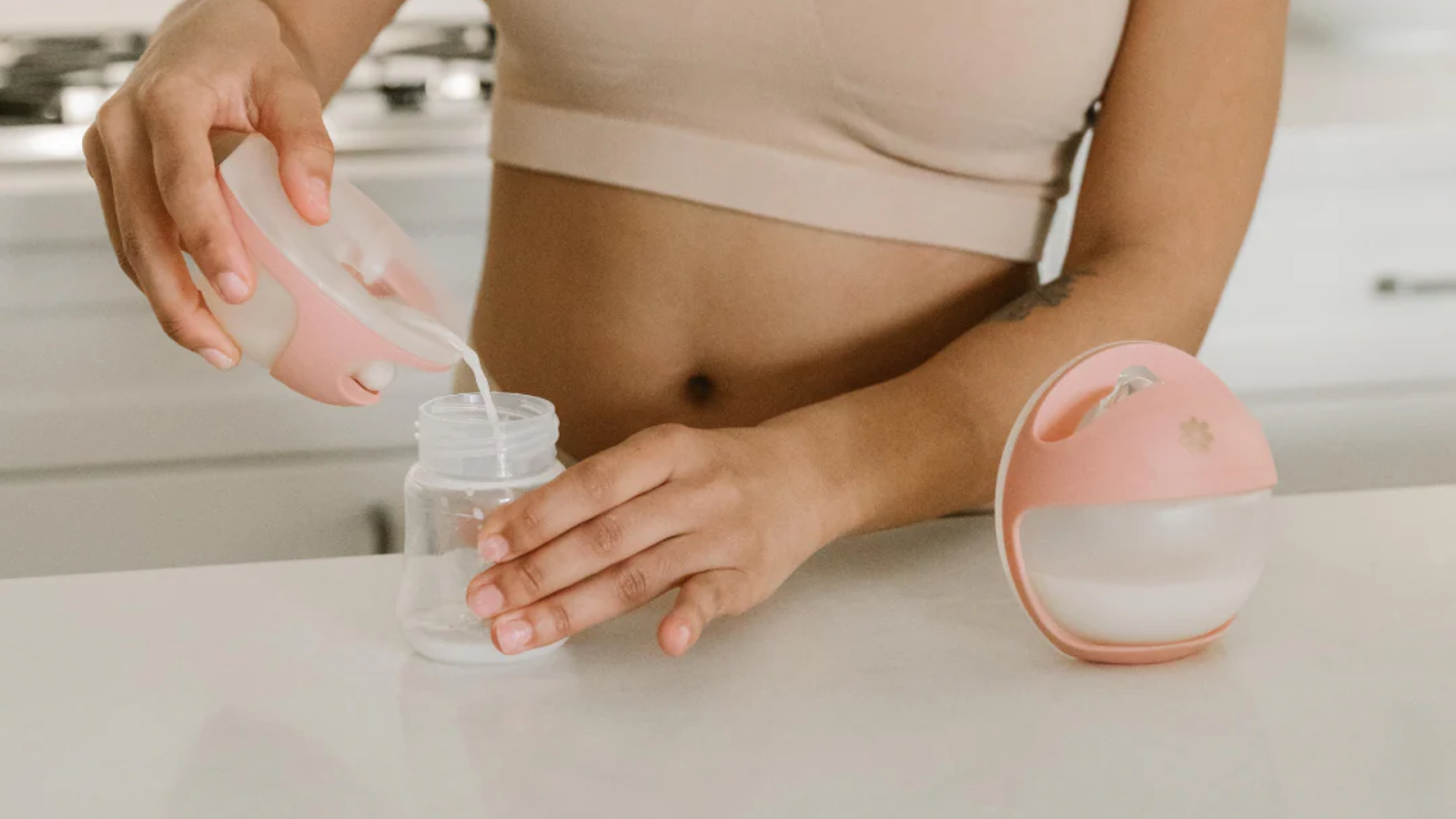 Mom pouring freshly pumped breast milk into a storage bottle after using a wearable breast pump at home.