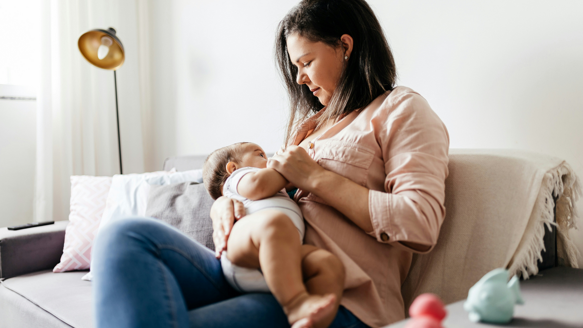 Mother breastfeeding her baby on the couch at home in a calm, natural moment.