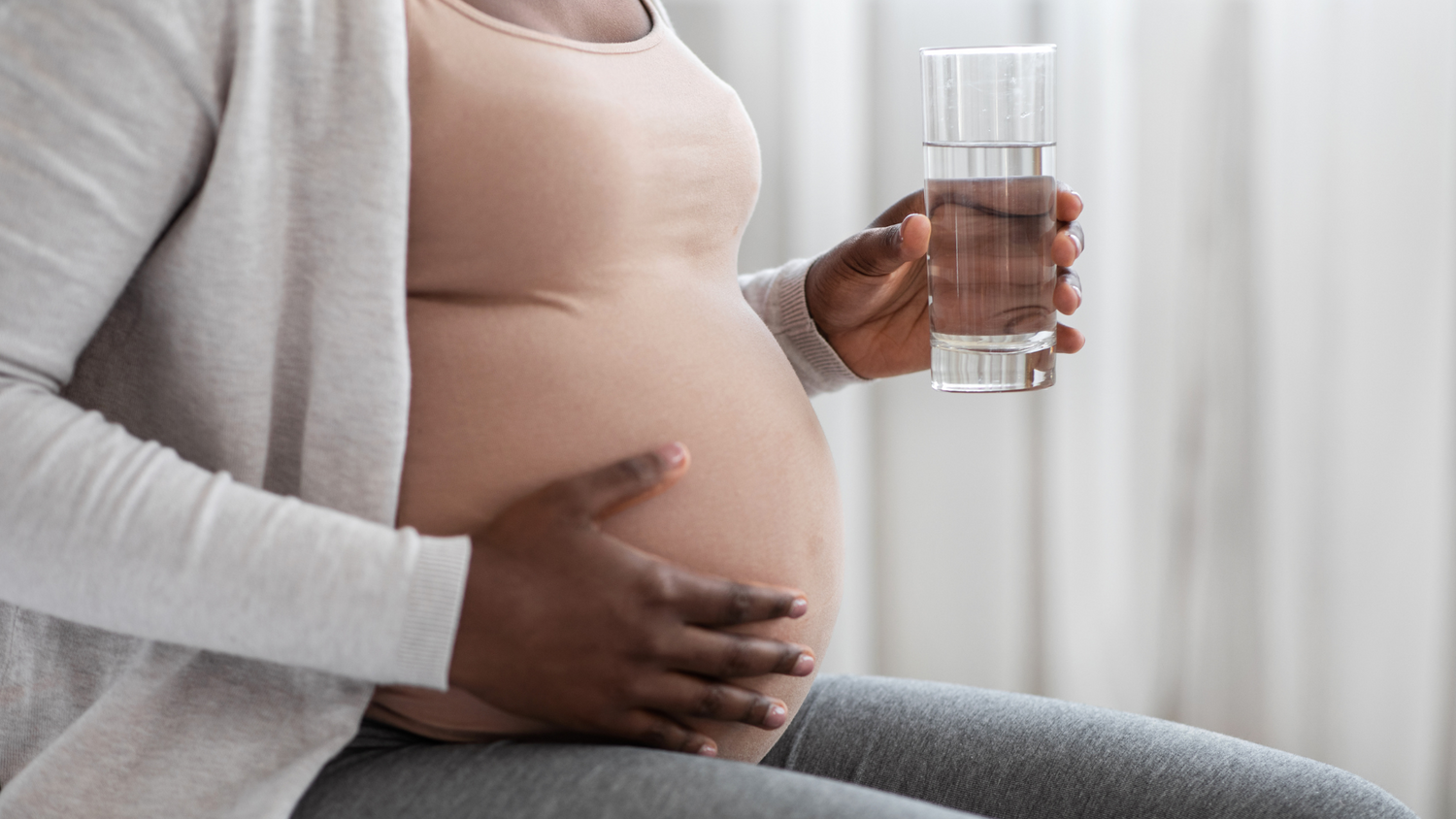 Pregnant woman holding a glass of water while cradling her belly.