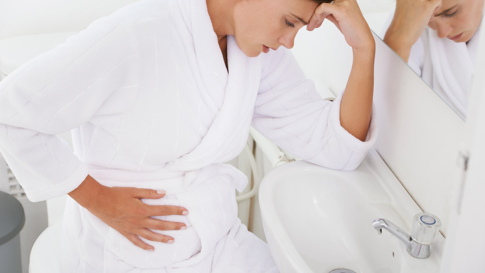 Pregnant woman in robe experiencing morning sickness near bathroom sink