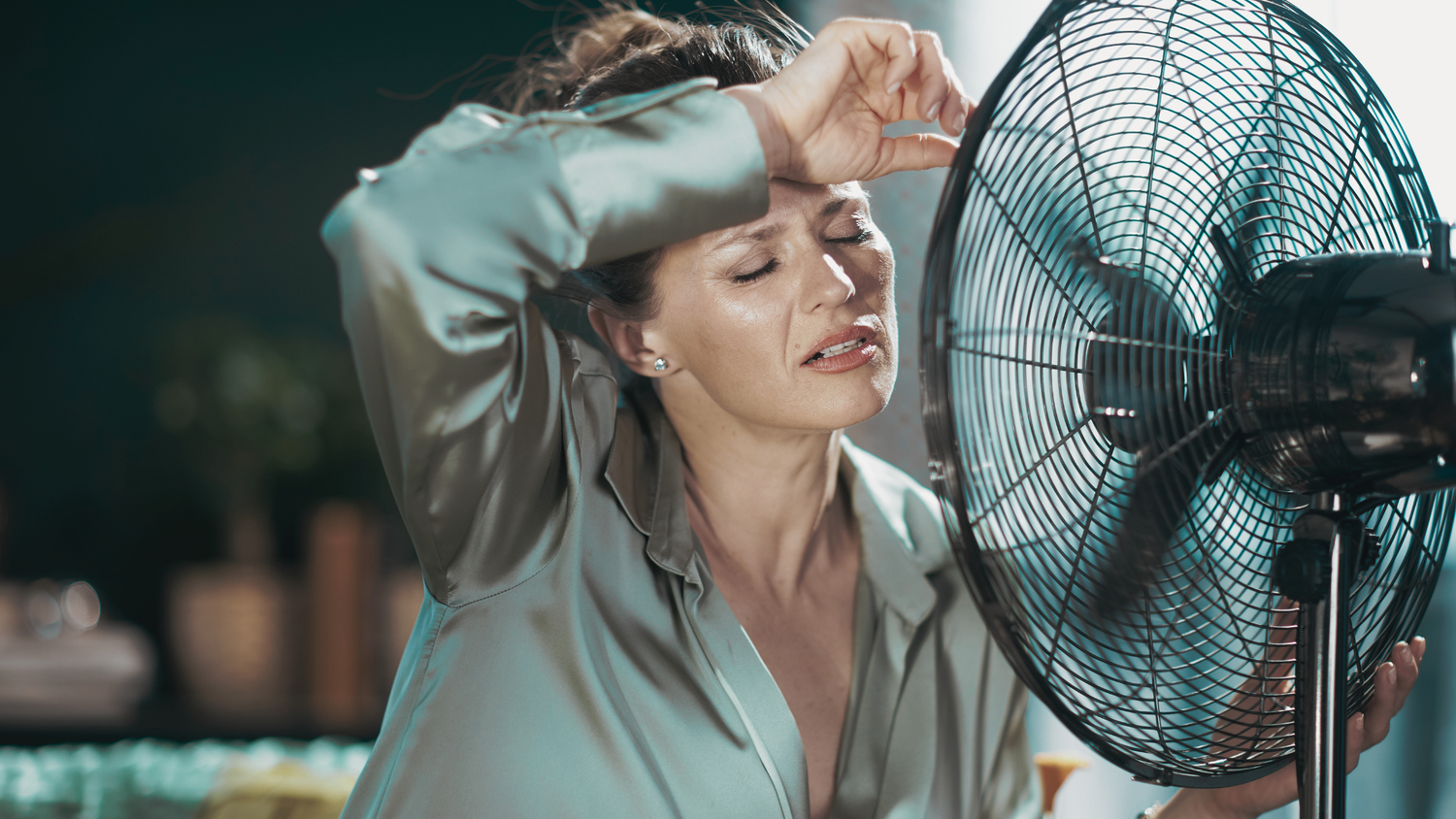 Woman sweating in front of fan experiencing postpartum night sweats