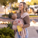 Mom carrying her baby in a soft carrier while drinking Boobie Protein Powder 