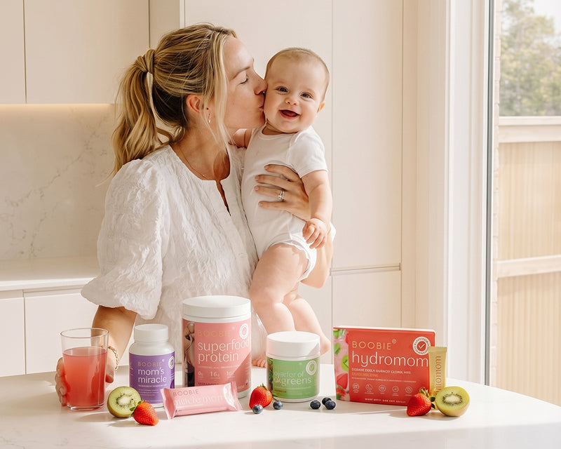 Woman holding a baby with Boobie* Superfoods health and wellness products on a table