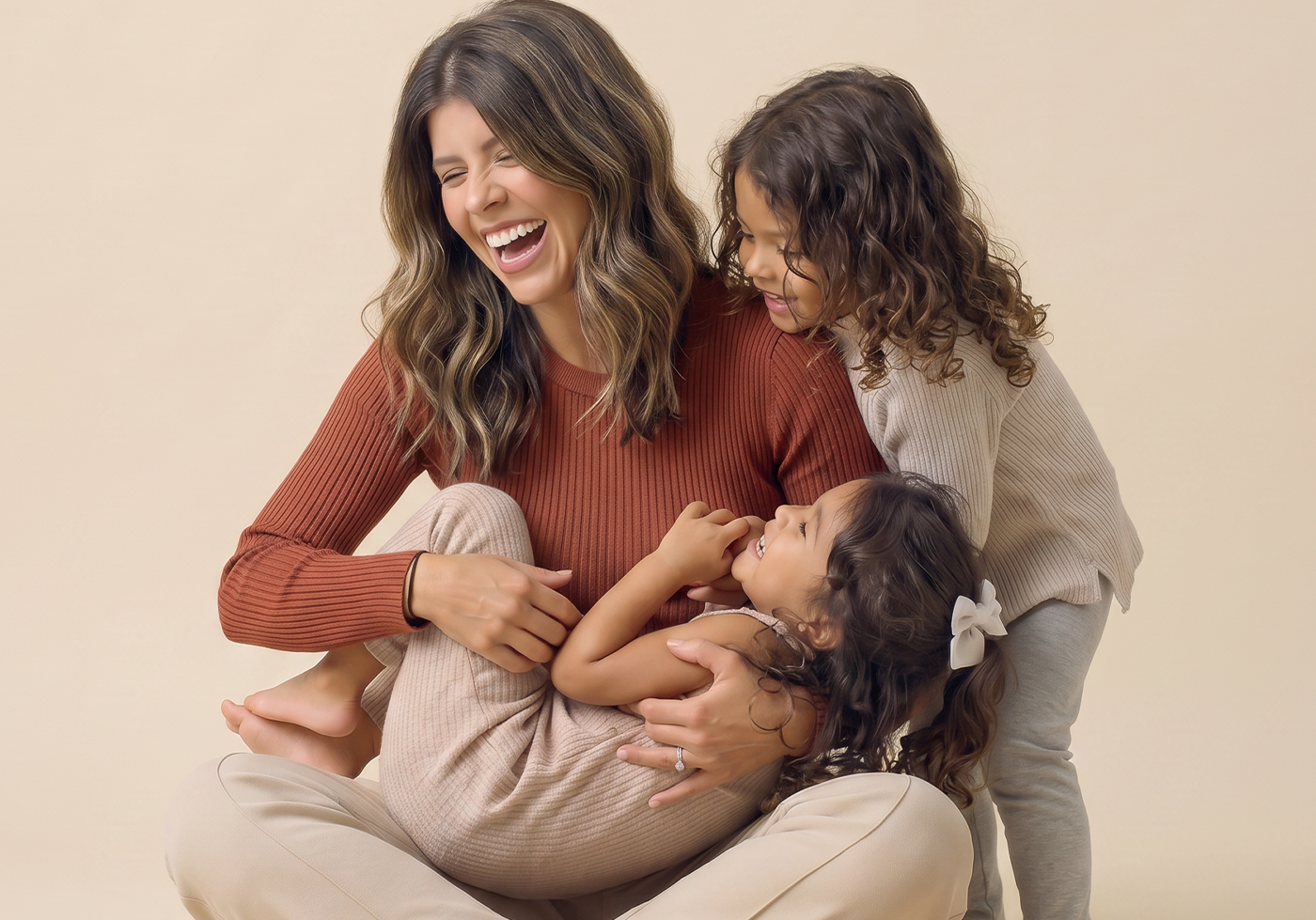 Woman sitting on a couch with two children, all smiling and laughing against a beige background