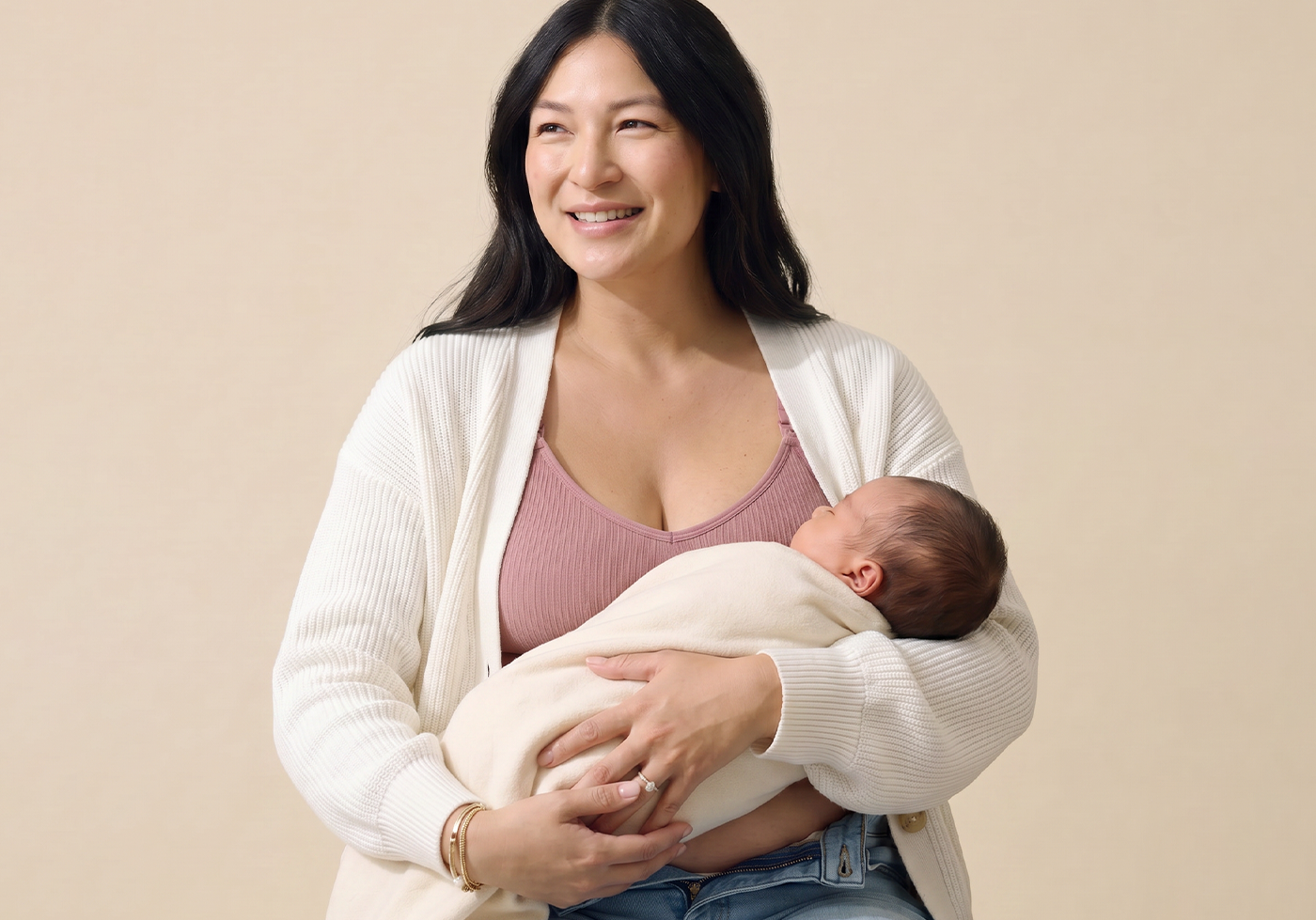 Woman holding a baby wrapped in a white blanket against a beige background