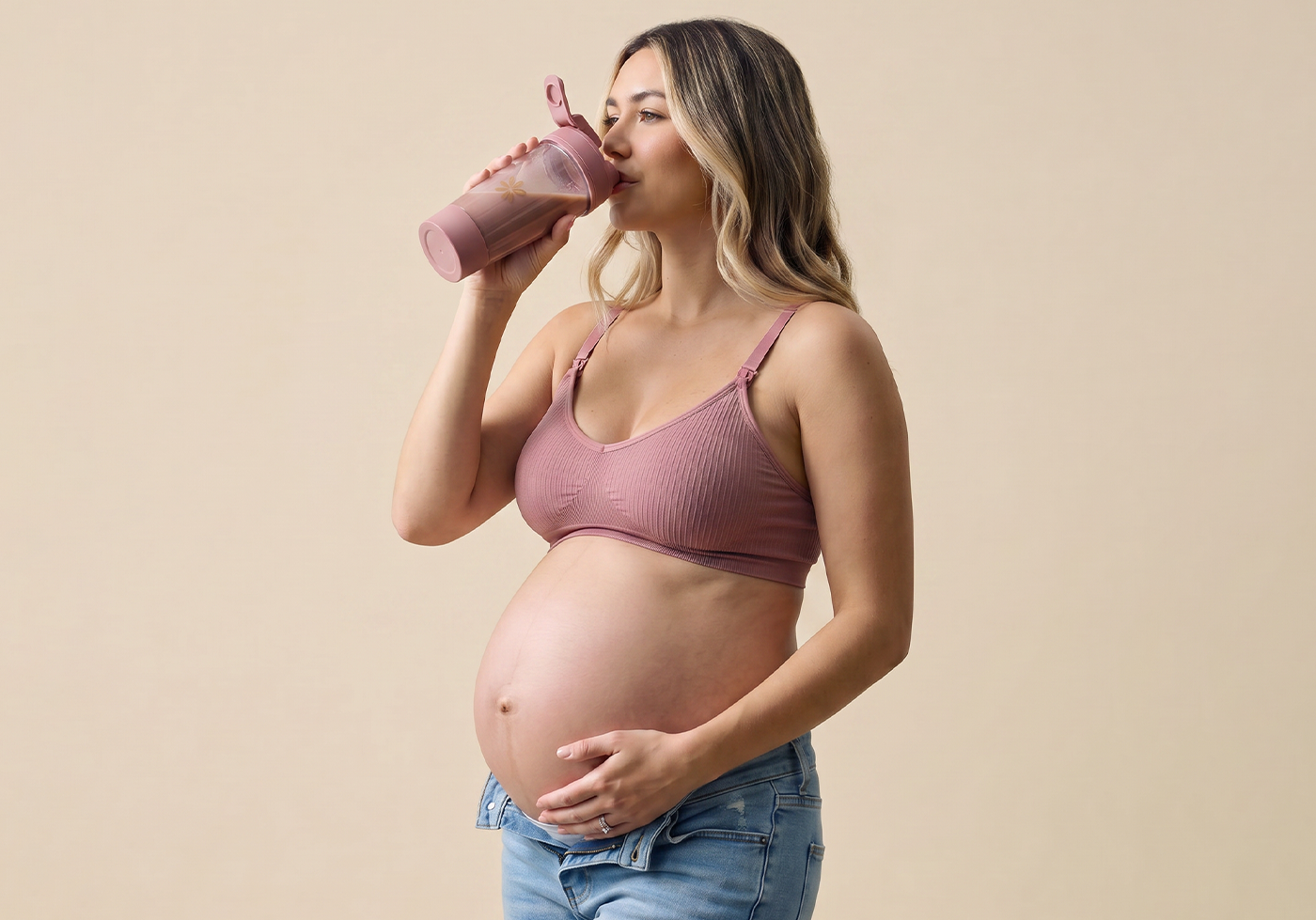 Pregnant woman drinking from a pink cup against a beige background